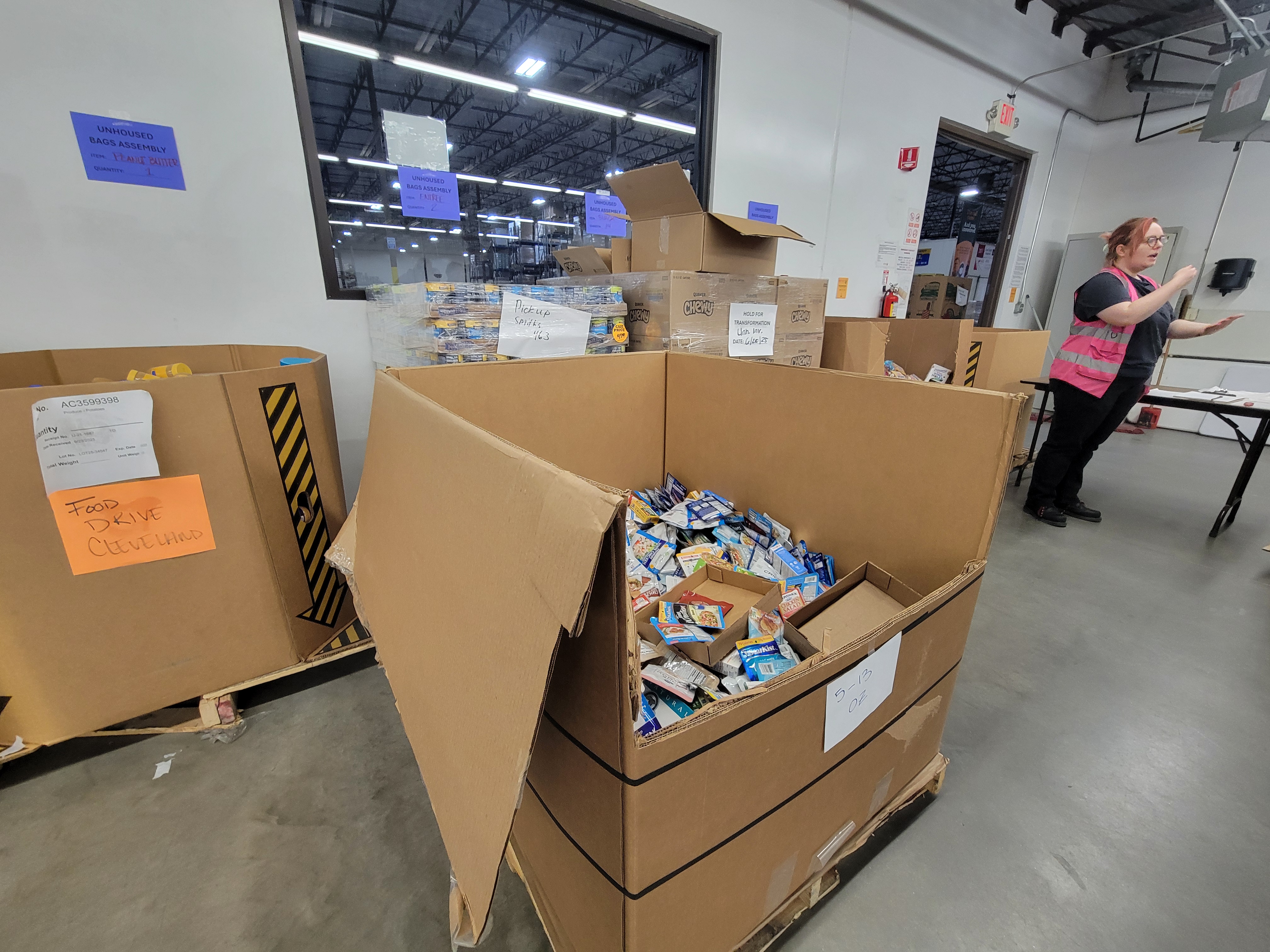 Cardboard containers and shelves of food for unhoused bag assembly line.